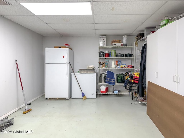 basement with white refrigerator, refrigerator, and a paneled ceiling