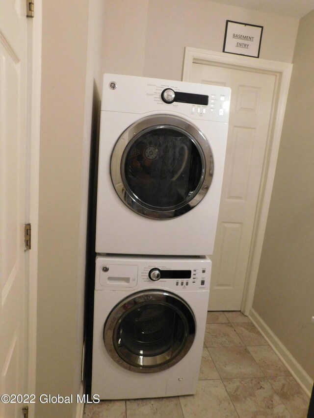 laundry area with stacked washer and dryer and light tile patterned flooring