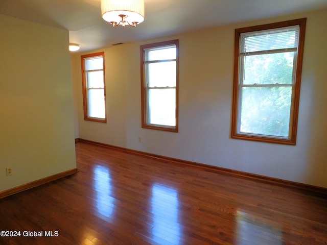 empty room featuring plenty of natural light, dark hardwood / wood-style floors, and a chandelier