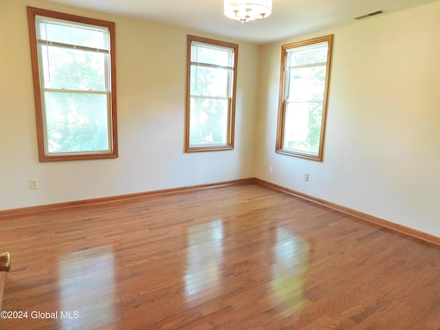 empty room with a chandelier, a healthy amount of sunlight, and light wood-type flooring