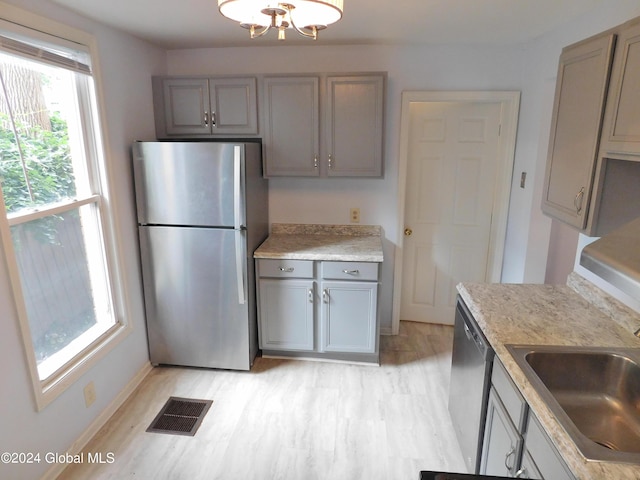 kitchen with sink, gray cabinets, appliances with stainless steel finishes, light hardwood / wood-style floors, and a chandelier