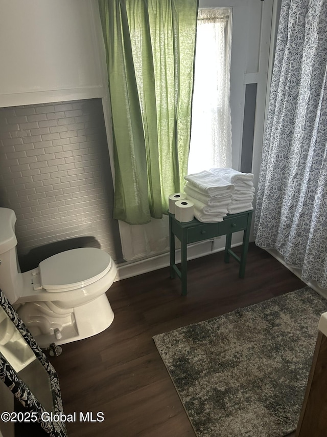 bathroom with hardwood / wood-style flooring, brick wall, and toilet