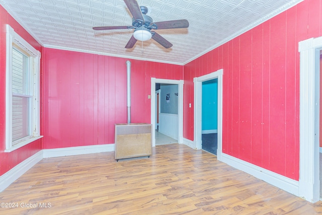 empty room with ceiling fan, hardwood / wood-style flooring, wooden walls, and ornamental molding