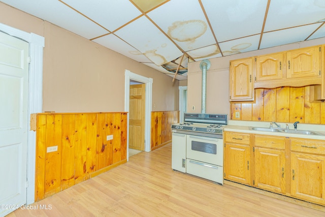 kitchen featuring light wood-type flooring, white gas range, wooden walls, and sink