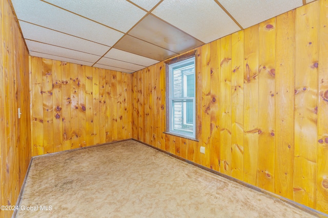 spare room featuring wooden walls, carpet flooring, and a paneled ceiling