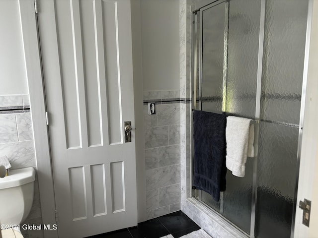 bathroom with tile patterned floors, a shower with door, toilet, and tile walls