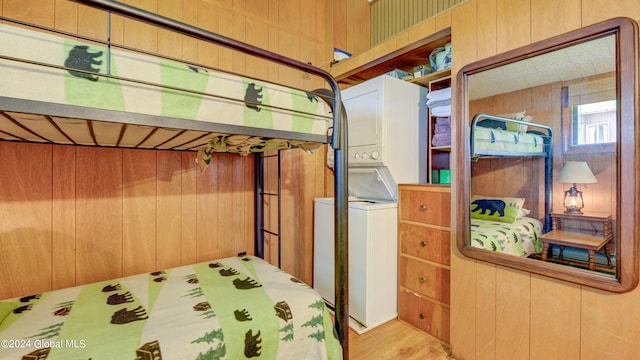 bedroom featuring estacked washer and dryer, wooden walls, and wood finished floors