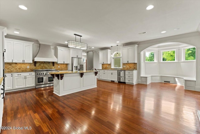 kitchen with appliances with stainless steel finishes, custom range hood, a kitchen island, white cabinets, and decorative light fixtures