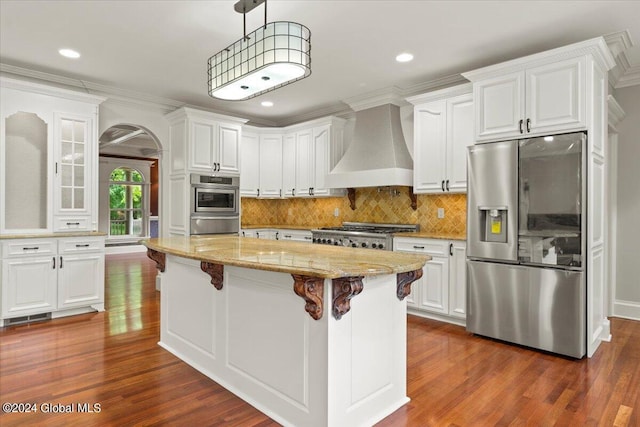 kitchen with premium range hood, a kitchen island, stainless steel refrigerator with ice dispenser, white cabinets, and decorative light fixtures