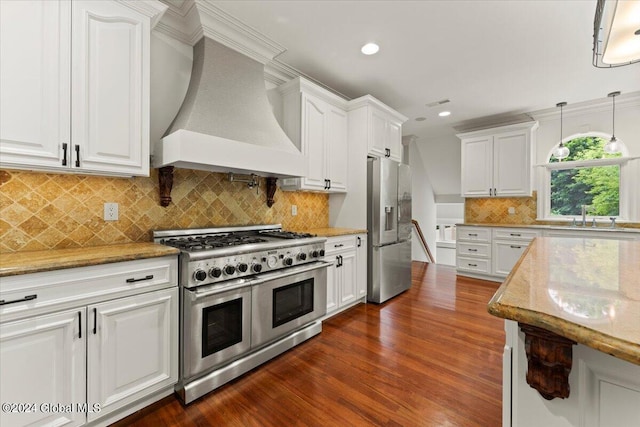 kitchen with light stone countertops, decorative light fixtures, white cabinets, custom exhaust hood, and appliances with stainless steel finishes