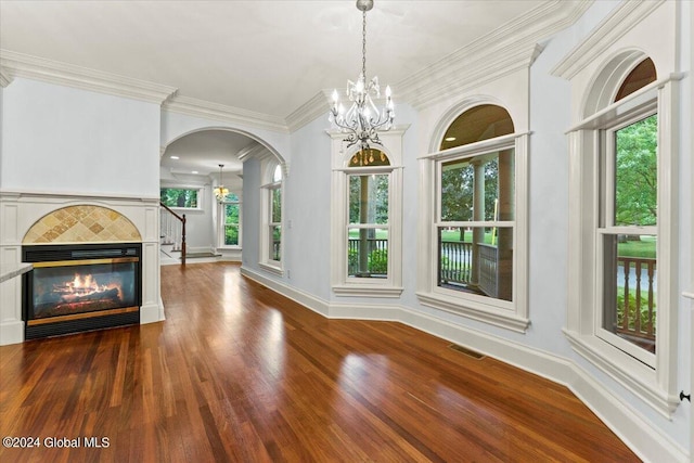 unfurnished dining area featuring a tiled fireplace, crown molding, a chandelier, and dark hardwood / wood-style floors