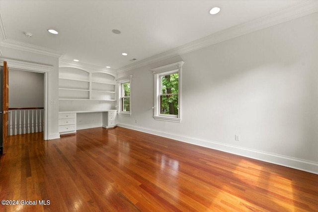 unfurnished living room featuring built in desk, hardwood / wood-style floors, crown molding, and built in shelves