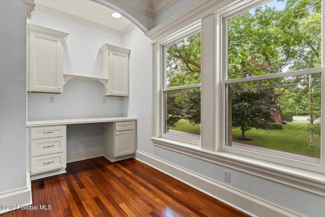 unfurnished office featuring built in desk, ornamental molding, and dark hardwood / wood-style floors