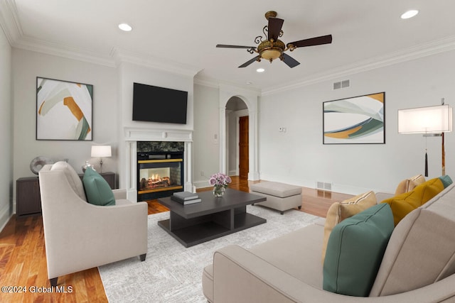 living room featuring ceiling fan, a premium fireplace, crown molding, and wood-type flooring