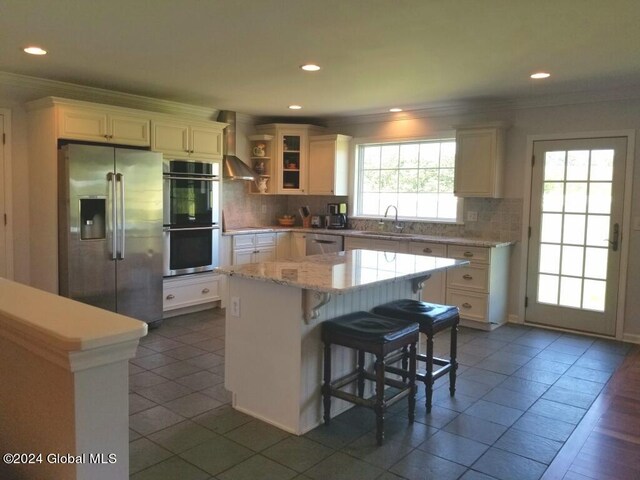 kitchen with a center island, wall chimney exhaust hood, backsplash, and appliances with stainless steel finishes