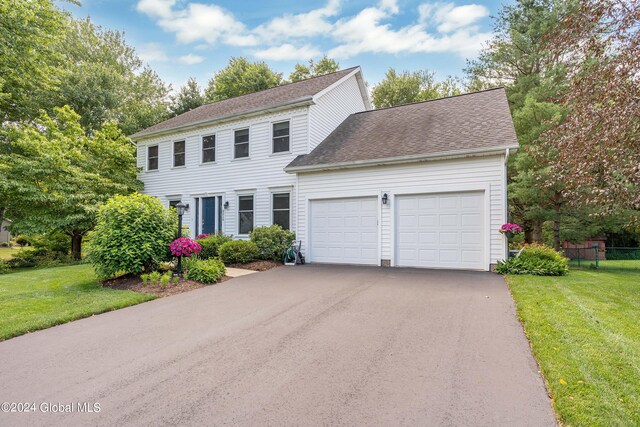 colonial-style house with fence, an attached garage, driveway, and a front lawn