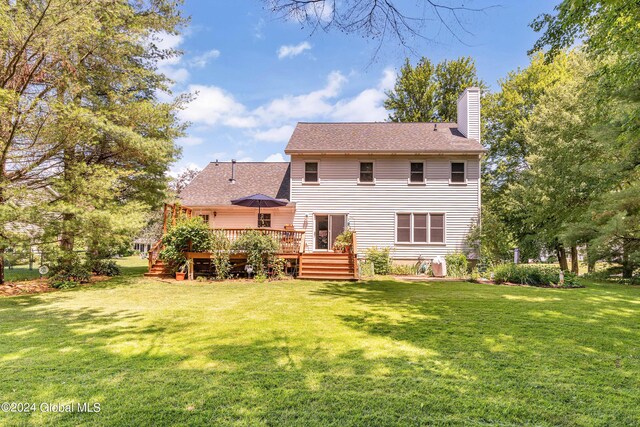rear view of property featuring a lawn, a wooden deck, a chimney, and roof with shingles