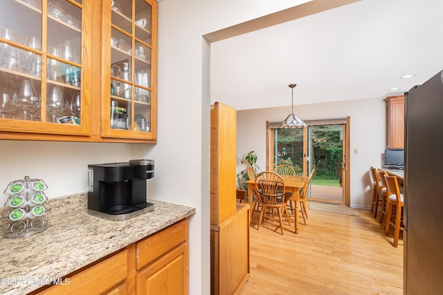 kitchen with light stone countertops, light wood-style flooring, recessed lighting, decorative light fixtures, and glass insert cabinets