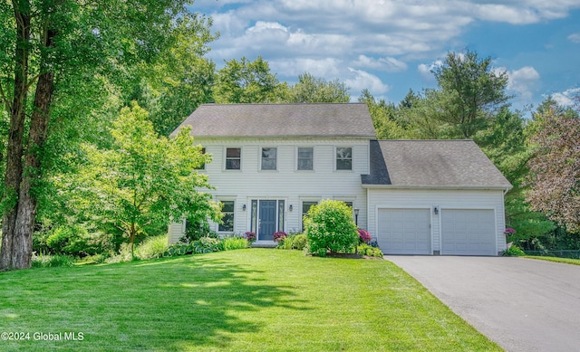 colonial house featuring a garage, a front yard, roof with shingles, and aphalt driveway