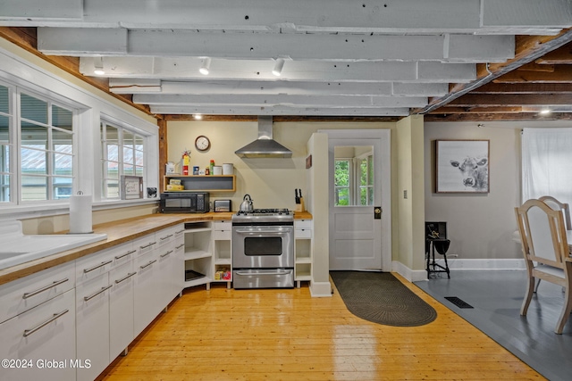 kitchen with wall chimney range hood, plenty of natural light, gas range, white cabinetry, and light wood-type flooring