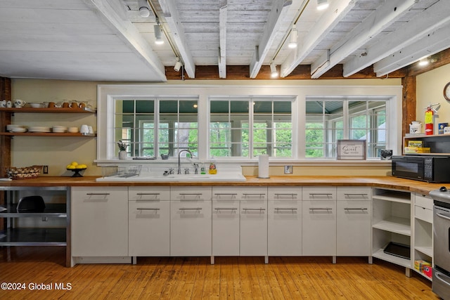 kitchen with light hardwood / wood-style floors, white cabinetry, stove, beamed ceiling, and sink