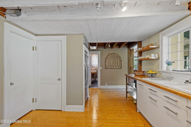 kitchen with white cabinets, beam ceiling, and light wood-type flooring