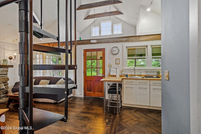 interior space featuring dark parquet floors, beamed ceiling, high vaulted ceiling, sink, and white cabinetry