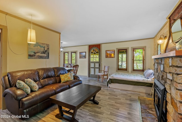 living room with crown molding, a stone fireplace, and hardwood / wood-style floors