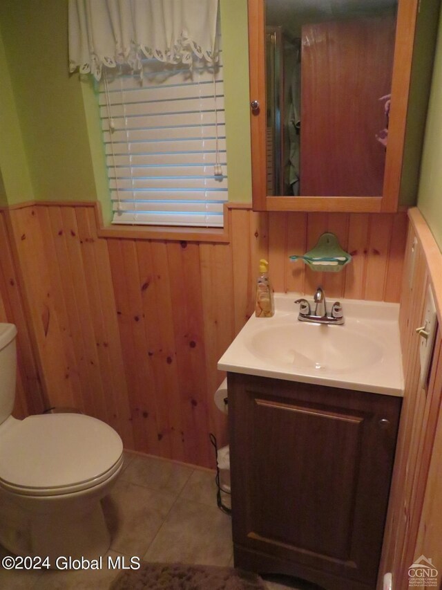 bathroom with wood walls, tile flooring, vanity, and toilet