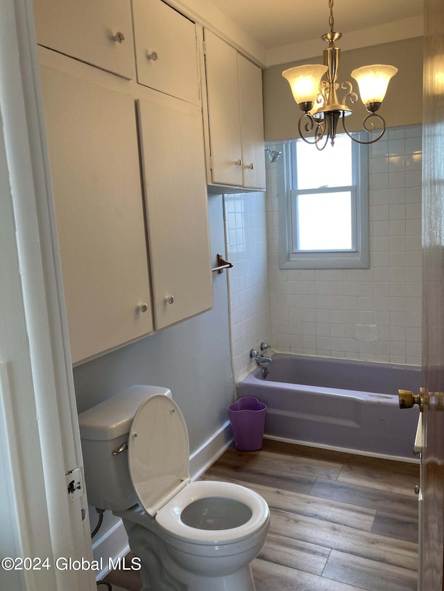 bathroom with wood-type flooring, toilet, tiled shower / bath, and a notable chandelier