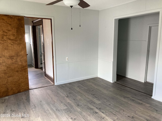 unfurnished bedroom featuring a closet, wood walls, ceiling fan, and dark hardwood / wood-style floors