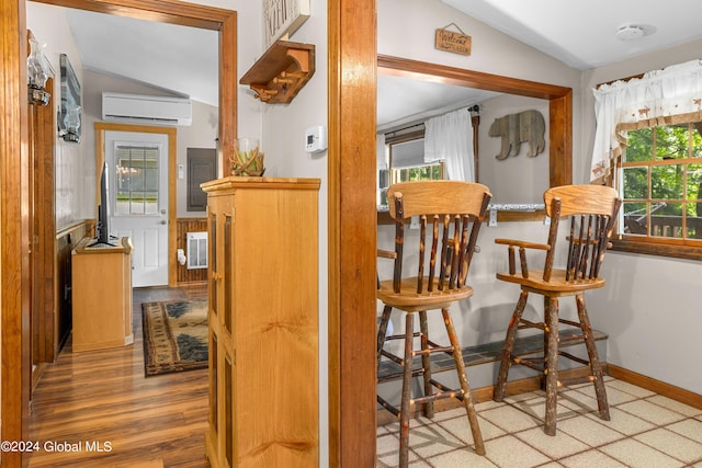 bar featuring vaulted ceiling, a wall mounted air conditioner, light hardwood / wood-style floors, and plenty of natural light