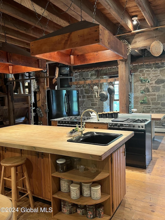 kitchen with sink, butcher block countertops, light wood-type flooring, black refrigerator, and stove