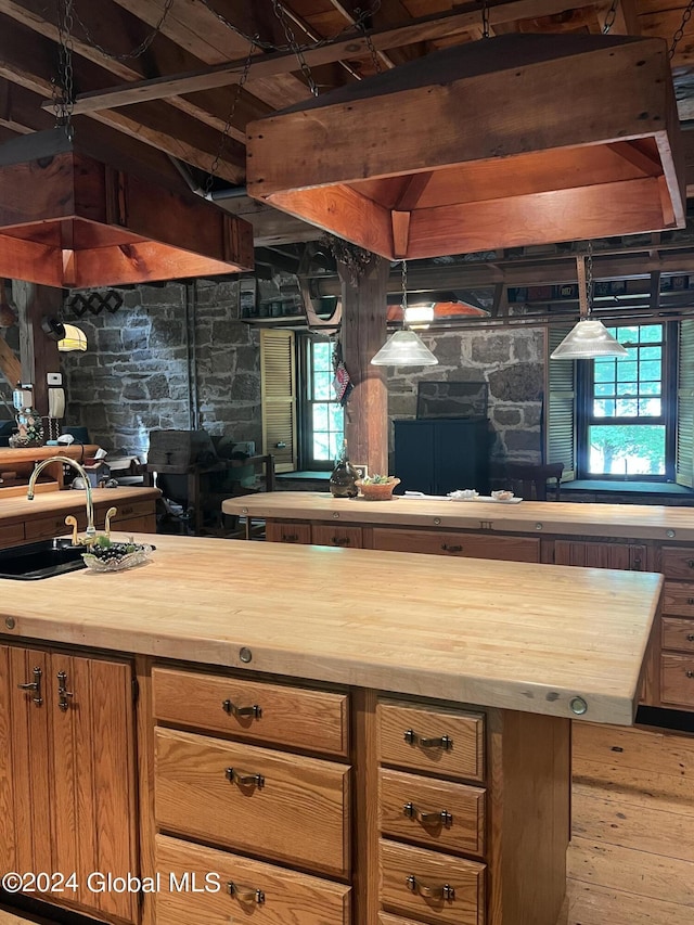 interior space featuring beam ceiling, butcher block countertops, sink, and hanging light fixtures