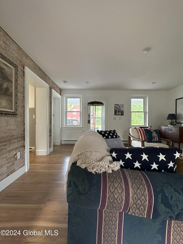 bedroom with brick wall, multiple windows, a baseboard heating unit, and wood finished floors