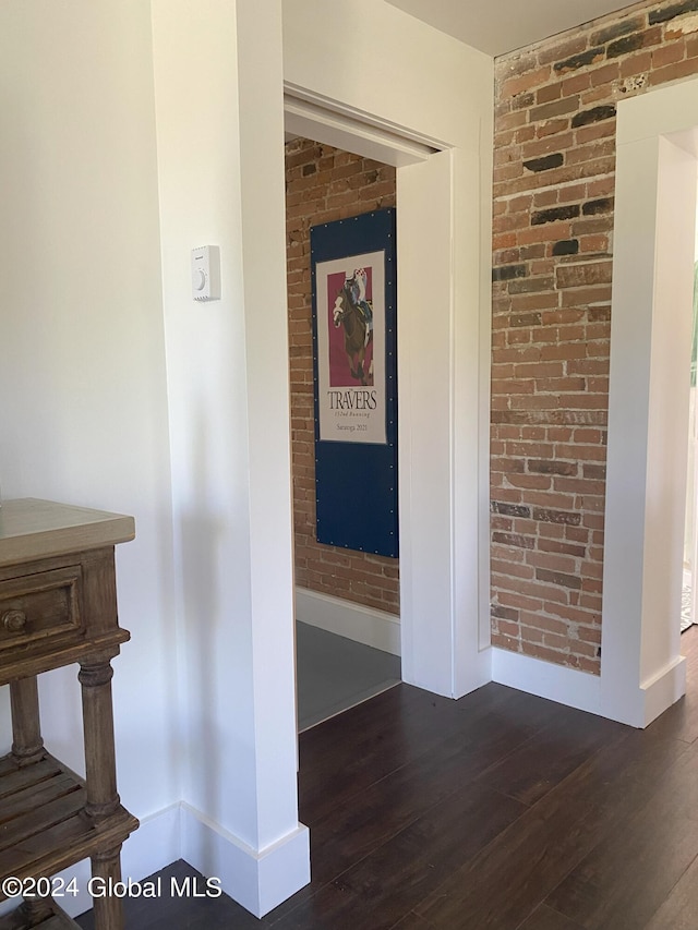 interior space with brick wall, dark wood-type flooring, and baseboards