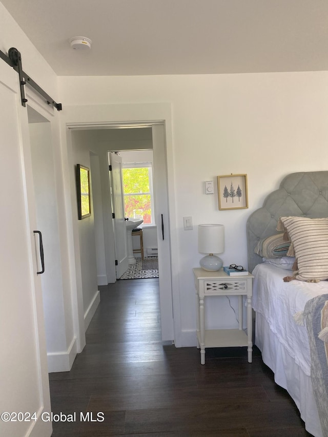 bedroom featuring a barn door, dark wood-type flooring, and baseboards