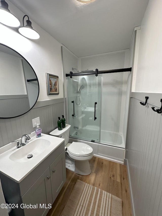 bathroom with toilet, a wainscoted wall, shower / bath combination with glass door, wood finished floors, and vanity