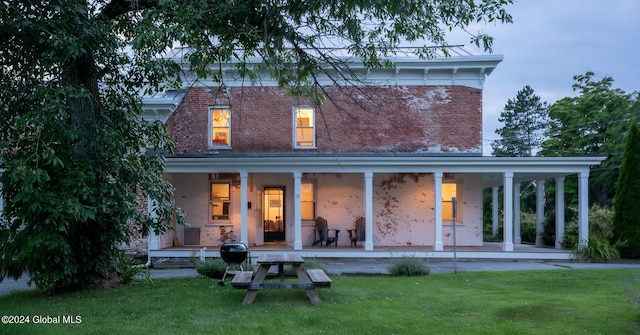 back of house featuring covered porch, a yard, and brick siding