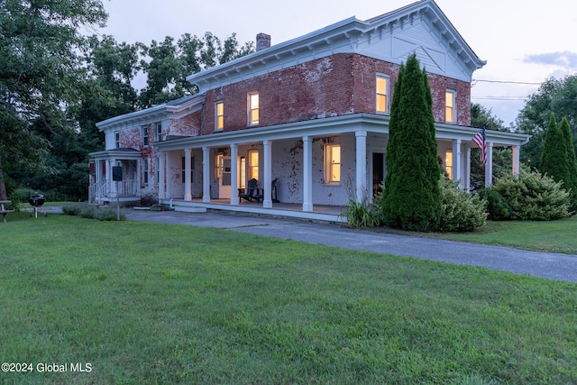 italianate-style house with a chimney, a front lawn, a porch, and brick siding