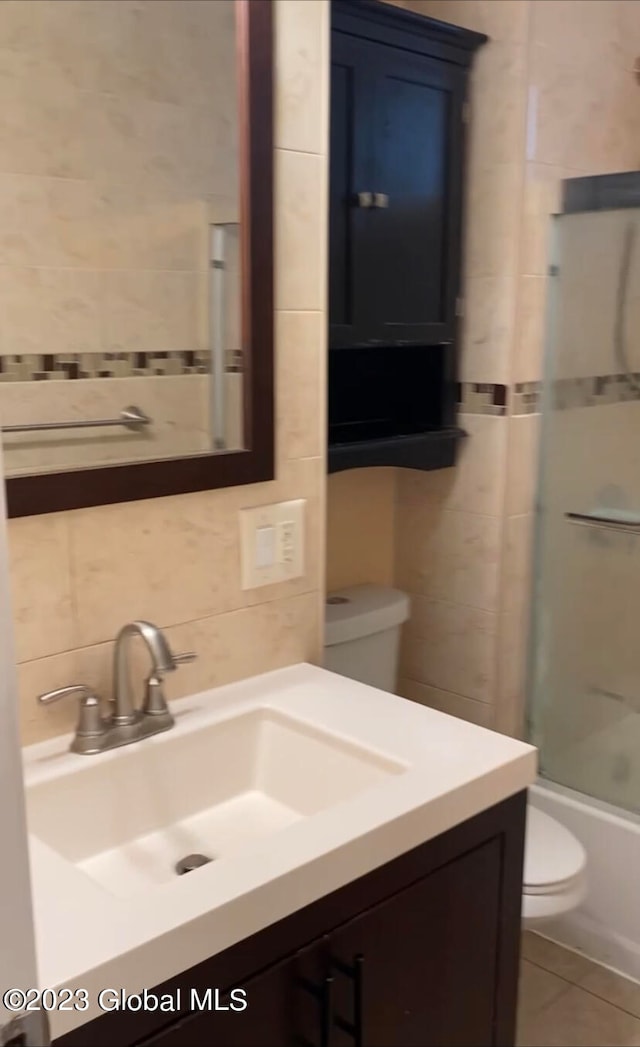 full bathroom featuring tile walls, shower / bath combination with glass door, vanity, and toilet