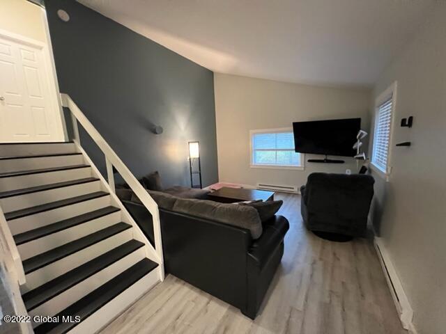 living room with a baseboard heating unit, lofted ceiling, and wood-type flooring