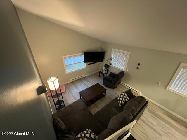 living room with lofted ceiling, baseboard heating, and light wood-type flooring