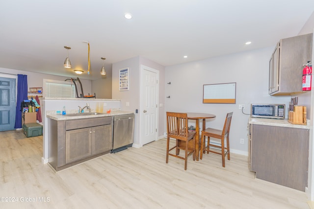 kitchen featuring sink, appliances with stainless steel finishes, pendant lighting, and light hardwood / wood-style floors