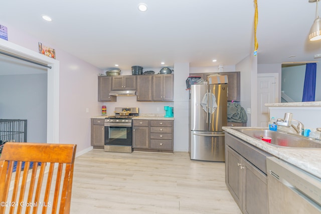 kitchen with sink, hanging light fixtures, stainless steel appliances, and light hardwood / wood-style floors