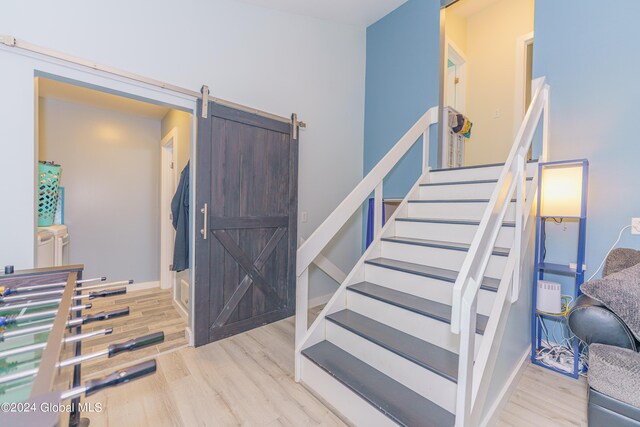 stairway featuring light wood-type flooring, washing machine and dryer, and a barn door