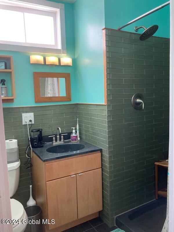 bathroom with tile patterned flooring, vanity, toilet, and tiled shower