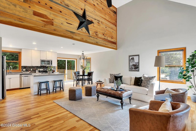 living room featuring sink, a towering ceiling, light hardwood / wood-style flooring, and a chandelier