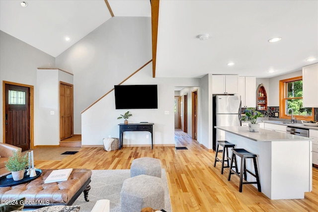 living room featuring high vaulted ceiling, sink, and light wood-type flooring