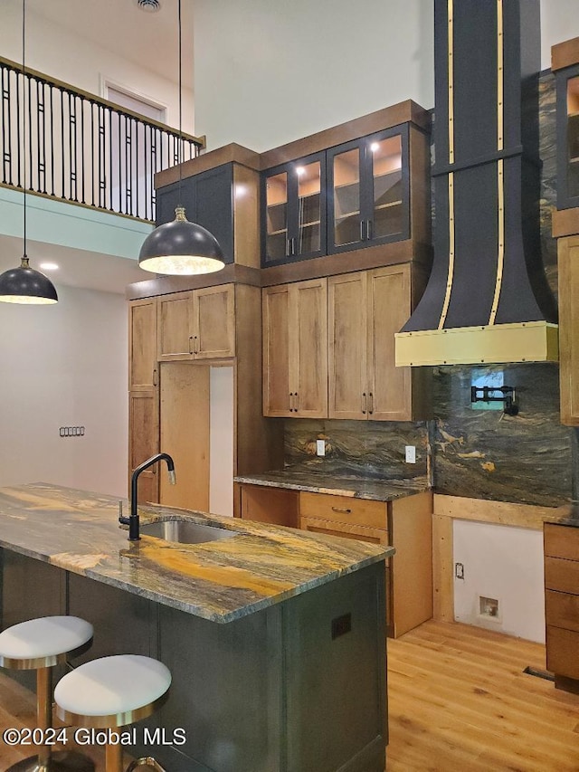 kitchen featuring sink, exhaust hood, dark stone countertops, pendant lighting, and a high ceiling